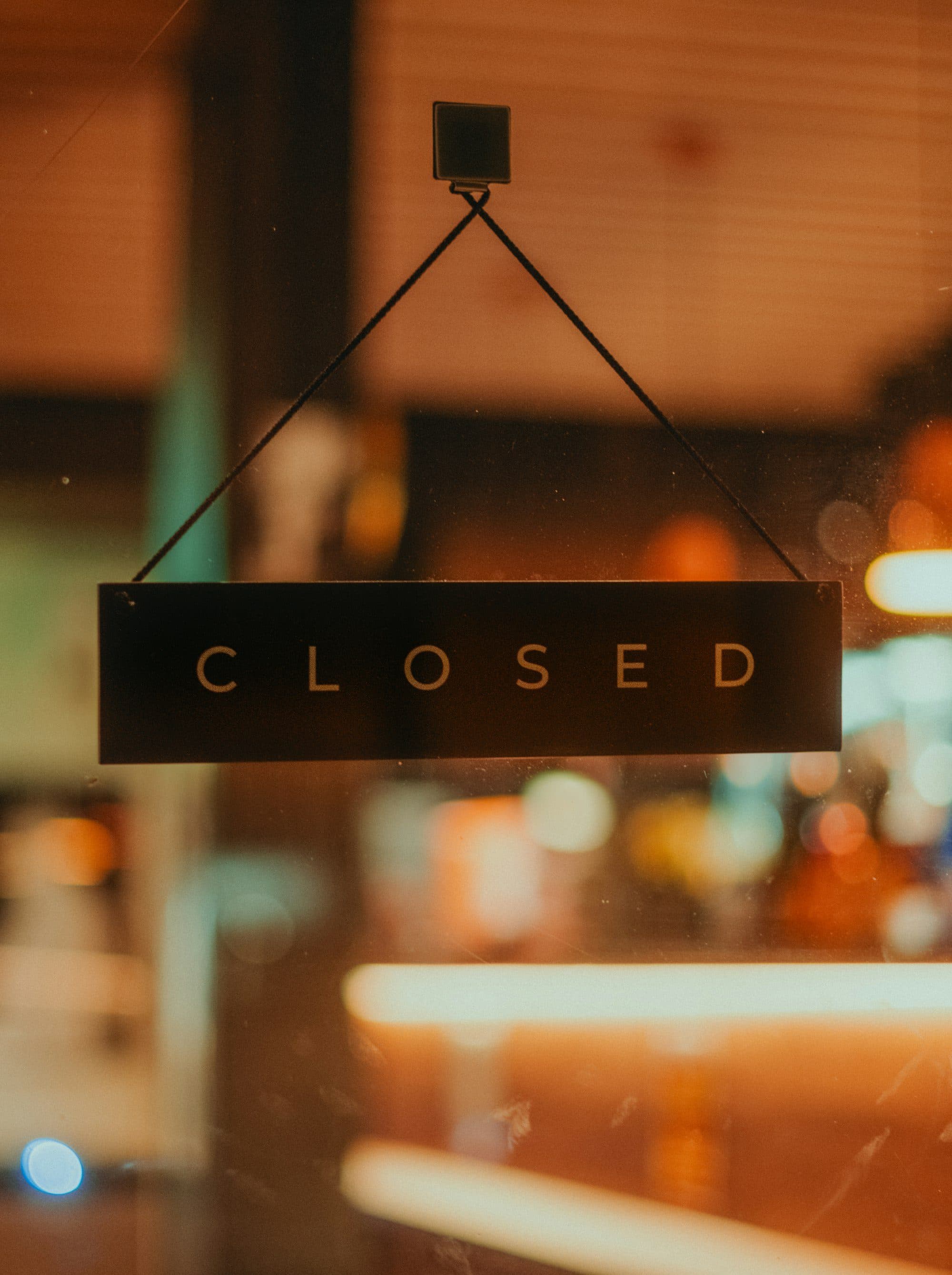 Une pancarte « Closed » pend derrière la vitrine d'un restaurant, le soir.